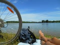 Summer landscape bike whell and barefoot legs girl resting on a lake blue sky background