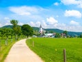 Summer landscape with lush green meadow, country road and white rural church. Prichovice, Northern Bohemia, Czech