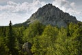 Summer landscape with majestic crest of grey rocky mountain and green forest in sunny day with sinlights and clouds in blue sky. Royalty Free Stock Photo