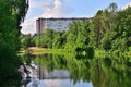 Summer landscape with pond surrounded by trees and multi-story building in the background Royalty Free Stock Photo