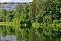 Summer landscape with pond surrounded by trees and multi-story building in the background Royalty Free Stock Photo