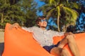 Summer lifestyle portrait of man sitting on the orange inflatable sofa on the beach of tropical island. Relaxing and Royalty Free Stock Photo