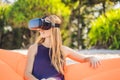 Summer lifestyle portrait of pretty girl sitting on the orange inflatable sofa and uses virtual reality headset on the Royalty Free Stock Photo