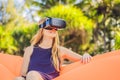 Summer lifestyle portrait of pretty girl sitting on the orange inflatable sofa and uses virtual reality headset on the Royalty Free Stock Photo