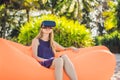 Summer lifestyle portrait of pretty girl sitting on the orange inflatable sofa and uses virtual reality headset on the Royalty Free Stock Photo