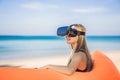 Summer lifestyle portrait of pretty girl sitting on the orange inflatable sofa and uses virtual reality headset on the Royalty Free Stock Photo