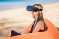 Summer lifestyle portrait of pretty girl sitting on the orange inflatable sofa and uses virtual reality headset on the Royalty Free Stock Photo