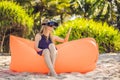 Summer lifestyle portrait of pretty girl sitting on the orange inflatable sofa and uses virtual reality headset on the Royalty Free Stock Photo