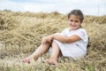 In summer a little girl is sits on a mown wheat field near the hay