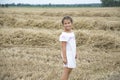 In summer a little girl is standing on a mown wheat field near the hay