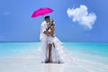 Summer love. Beautiful happy young couple in wedding clothes and pink umbrella is standing on a beach in the Maldives. Engagements Royalty Free Stock Photo