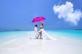 Summer love. Beautiful happy young couple in wedding clothes and pink umbrella is standing on a beach in the Maldives. Engagements Royalty Free Stock Photo