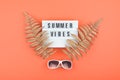 Summer luxury flat lay on coral background with Summer vibes text on light box, golden tropical leaves and white sunglasses