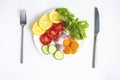 Summer menu, a plate of fresh vegetables, a fork and a knife on a white background, flat lay Royalty Free Stock Photo