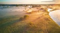 Summer misty sunrise on meadow. Country road on green fields riverbank