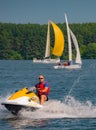 Summer mood: yellow and white sails on the blue sky background and a man on a yellow scooter .