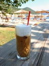 Summer morning with freddo cappuccino greek cold coffee drink on the backgraund straw umbrellas and sunbeds of Antisamos beach, Royalty Free Stock Photo