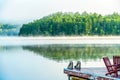 Early morning mist with dock and red wooden chairs Royalty Free Stock Photo