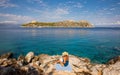 Summer morning young woman sunbathing and reading on a rocky beach of Agistri island, Aponissos bay, Saronic Gulf, Greece