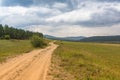 Summer mountain landscape. A rural road against the background of mountains in the Cis-Baikal basin. Irkutsk region, Russia Royalty Free Stock Photo