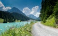 Summer mountain landscape with turquoise lake and gravel road bordered by wildflowers Royalty Free Stock Photo