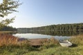 Summer nature. Landscape with lake water, forest on sky horizon, wood pier and boat on grass coast in morning Royalty Free Stock Photo