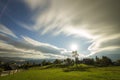 Summer night mountain panorama. Old wooden weathered shepherd huts on green clearing on cloudy evening sky background, bright road