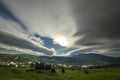 Summer night mountain panorama. Old wooden weathered shepherd huts on green clearing on cloudy evening sky background, bright road