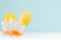 Summer orange lemonade with ice cube, slices oranges in misted glass on elegant pastel green wall, white wood table.