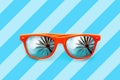 Summer orange sunglasses with palm trees reflections isolated in blue background with diagonal stripes Royalty Free Stock Photo