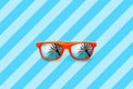 Summer orange sunglasses with palm trees reflections isolated in large blue background with diagonal stripes.