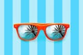 Summer orange sunglasses with palm trees reflections isolated in pastel blue background with stripes Royalty Free Stock Photo