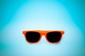 Summer orange sunglasses in vignetting blue background. Minimal concept image for sun protection