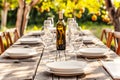 Summer outdoor party with wooden table with holiday table setting and bottle of wine