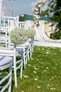 Summer outdoor wedding ceremony decoration. White chairs decorated with gypsophila balls on the background of the arch for the wed Royalty Free Stock Photo