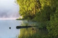 Summer pastoral landscape, fishing pier on a quiet lake in the fog in early morning