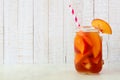 Summer peach iced tea in a mason jar glass against white wood