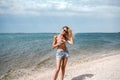 Summer photo of blonde happy woman relaxing on the beach, smiling. Girl with fit tan body wearing short jeans Royalty Free Stock Photo