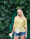 Outdoors portrait of young beautiful blonde woman with high bun hairstyle jeans shorts yellow blouse enjoying journey weekend posi