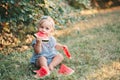 Summer picnic food. Cute Caucasian baby girl eating ripe red watermelon in park. Funny child kid sitting on ground with fresh Royalty Free Stock Photo