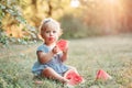 Summer picnic food. Cute Caucasian baby girl eating ripe red watermelon in park. Funny child kid sitting on ground with fresh Royalty Free Stock Photo