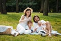 Summer picnic. Happy parents with two kids dressed in white casual clothes are sitting on the coverlet on green grass.