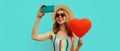 Summer portrait beautiful smiling young woman taking a selfie by smartphone with red heart shaped balloon wearing a sunglasses Royalty Free Stock Photo