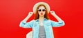 Summer portrait of beautiful young woman wearing summer straw hat, jeans jacket and backpack on red background Royalty Free Stock Photo