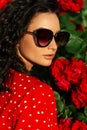 Summer portrait of fashion pretty woman with stylish sunglasses in red dress near flowers of roses Royalty Free Stock Photo