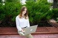Summer portrait of a female freelancer sitting on a park bench outdoors while working on a laptop. Royalty Free Stock Photo