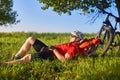 Summer portrait of handsome young man lying on green meadow near bike and backpack.