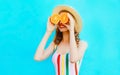 Summer portrait happy smiling woman holding in her hands two slices of orange fruit hiding her eyes in straw hat on colorful blue Royalty Free Stock Photo