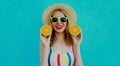 Summer portrait happy smiling woman holding in her hands two slices of orange fruit in straw hat on a colorful blue background Royalty Free Stock Photo