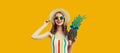 Summer portrait of happy smiling woman with pineapple wearing sunglasses, straw hat posing on yellow background Royalty Free Stock Photo